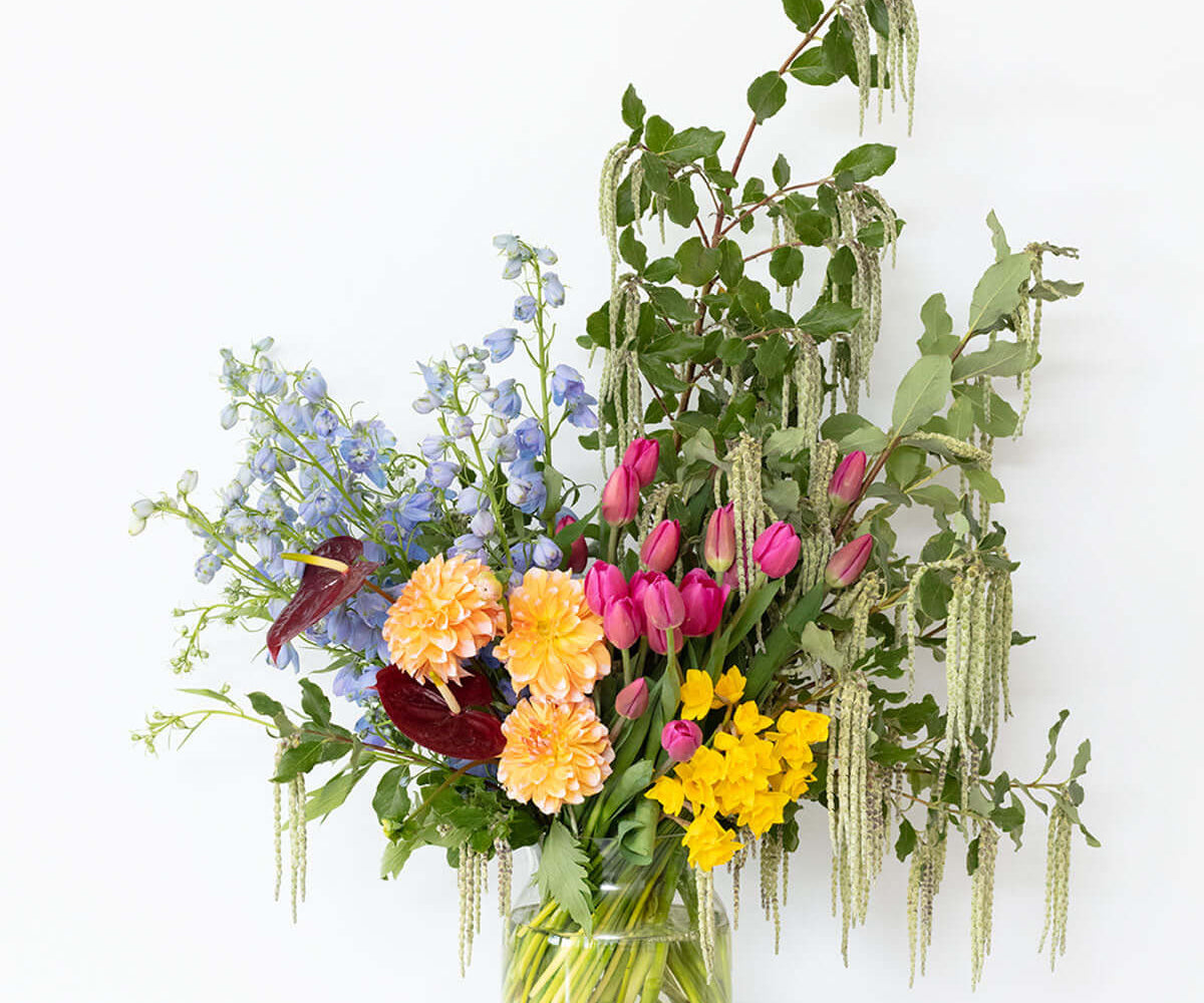 Vibrant Jewels Bouquet showcasing bright flowers in a glass vase against a simple background.