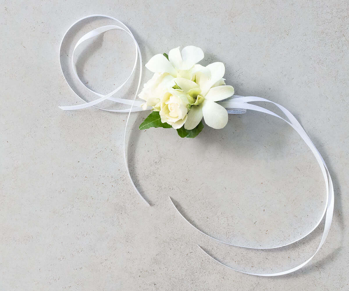 Singapore Orchid and Rose Corsage with white ribbon and delicate flowers on a smooth surface.